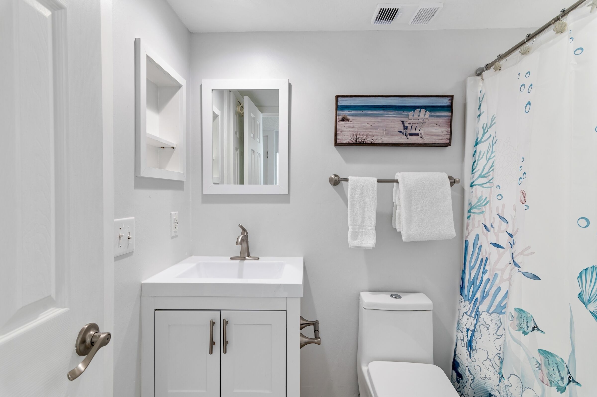 A bathroom with a white sink, a toilet, a mirror, and a shower curtain with a sea-themed design.