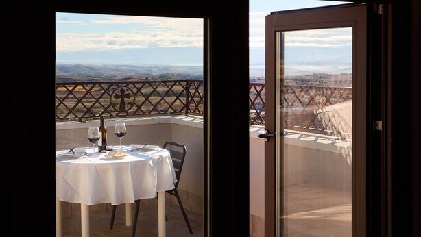 Ein Balkon mit Tisch für zwei Personen, einer Weinflasche und einem Kreuz.
