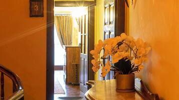 A hallway with a wooden staircase, a vase of white flowers, and a wall-mounted light fixture.