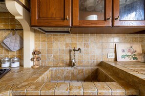 A kitchen with wooden cabinets, a tiled backsplash, a sink, and a wall-mounted faucet. - [St. Peter's view point] Elegant apartment (Roma)