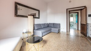A modern living room with a grey sectional sofa, a round coffee table, a white bed, a small side table, and a large mirror on the wall. - [St. Peter's view point] Elegant apartment (Roma)