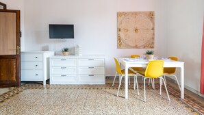 A dining area with a white table, yellow chairs, a TV mounted on the wall, and a patterned floor. - [St. Peter's view point] Elegant apartment (Roma)