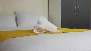 A neatly made bed with a yellow bedspread and a rolled white towel on top. - Kunda House Bournbrook (Birmingham)