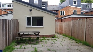 A small, single-story building with a wooden fence, a window, and a picnic table. - Kunda House Bournbrook (Birmingham)