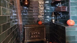 A narrow, tiled bathroom with a rustic design, featuring a wooden shelf with bottles and a decorative lantern.
