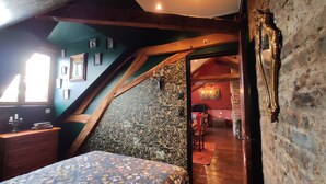 A bedroom with a sloped ceiling, wooden beams, a bed with a floral bedspread, a small desk, and a window.