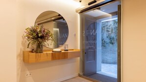 Un interior moderno con una consola de madera, un espejo redondo y un jarrón con flores.