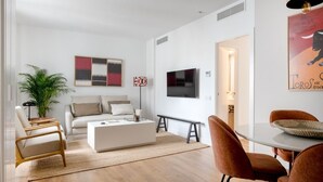 Una sala de estar moderna con un sofá blanco, una mesa de centro y un televisor montado en la pared. Hay un comedor con una mesa y sillas.