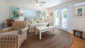 A living room with a striped sofa, a white bench, a round coffee table, and a ceiling fan. - Perfect Island Location! Heated pool and plenty of room for the entire family (Anna Maria)