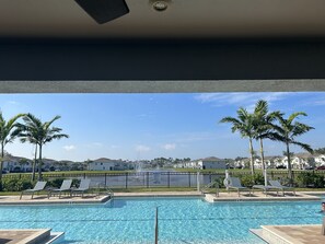 A swimming pool with lounge chairs, palm trees, and a view of houses in the background. - Centrally Located Cozy Condo (Naples)