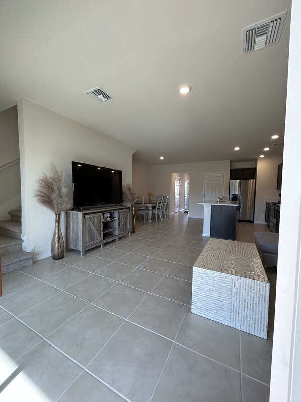 A spacious living area with a flat-screen TV, a dining table, and chairs. There is a kitchen area with a refrigerator and a sink. - Centrally Located Cozy Condo (Naples)