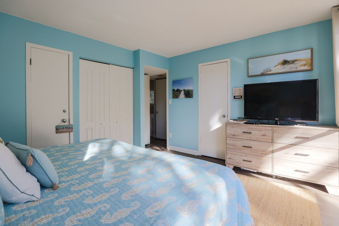 A bedroom with a bed, a dresser, a television, and a door.