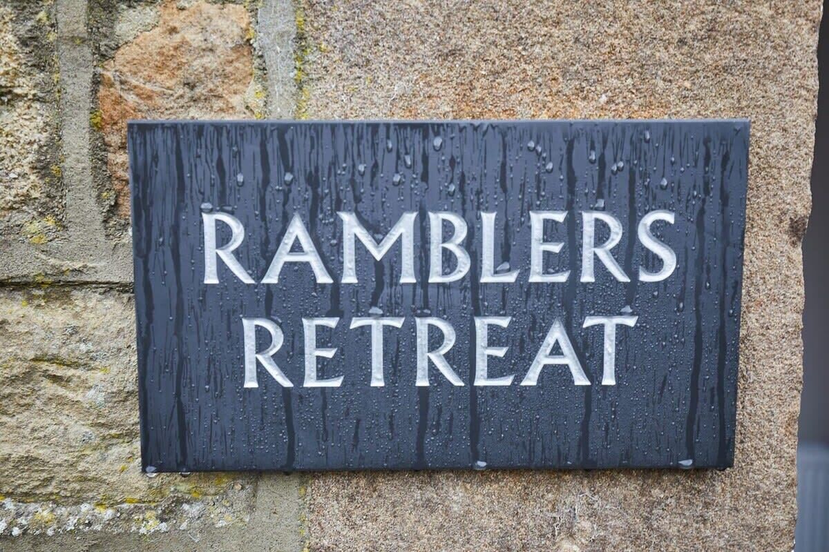 A sign reading "RAMBLERS RETREAT" mounted on a stone wall.