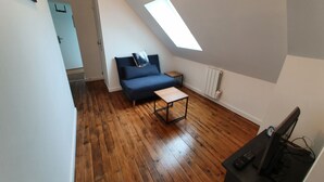 A small, modern room with a sloped ceiling, a blue sofa, a small table, and a TV. - Comfortable house 700m from the beach and 800m from the shops (Pénestin)