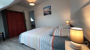 A bedroom with a bed, a bedside lamp, a painting on the wall, and a door leading to another room. - Comfortable house 700m from the beach and 800m from the shops (Pénestin)