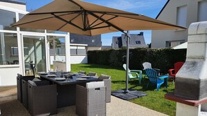 An outdoor patio area with a dining table set for four, surrounded by wicker furniture, under a large umbrella. - Comfortable house 700m from the beach and 800m from the shops (Pénestin)