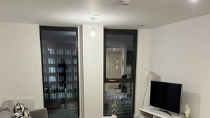 Ett modernt vardagsrum med en grå soffa, en mindre fåtölj, ett vitt soffbord och en TV-bänk med en platt-TV.