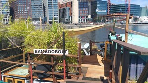 Ein Bambusboot liegt an einem Uferbereich, im Hintergrund moderne Gebäude.