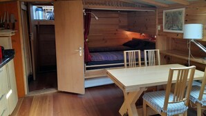 Eine gemütliche Holzhütte mit Essbereich, einer kleinen Küche und einem Schlafschlaf.