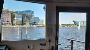 Blick aus einem Fenster auf einem Boot, mit Blick auf einen Fluss, moderne Gebäude und eine Brücke.