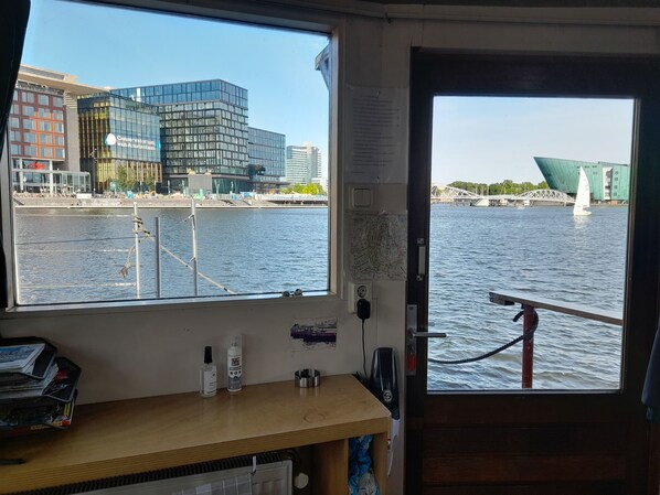 A view from a window on a boat, overlooking a river with modern buildings and a bridge. - Boat with a view in center of Amsterdam (Amsterdam)