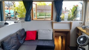Ein kompakter Wohnraum mit einer Couch, einem kleinen Tisch, einem Ventilator und einem Fenster mit Vorhängen.