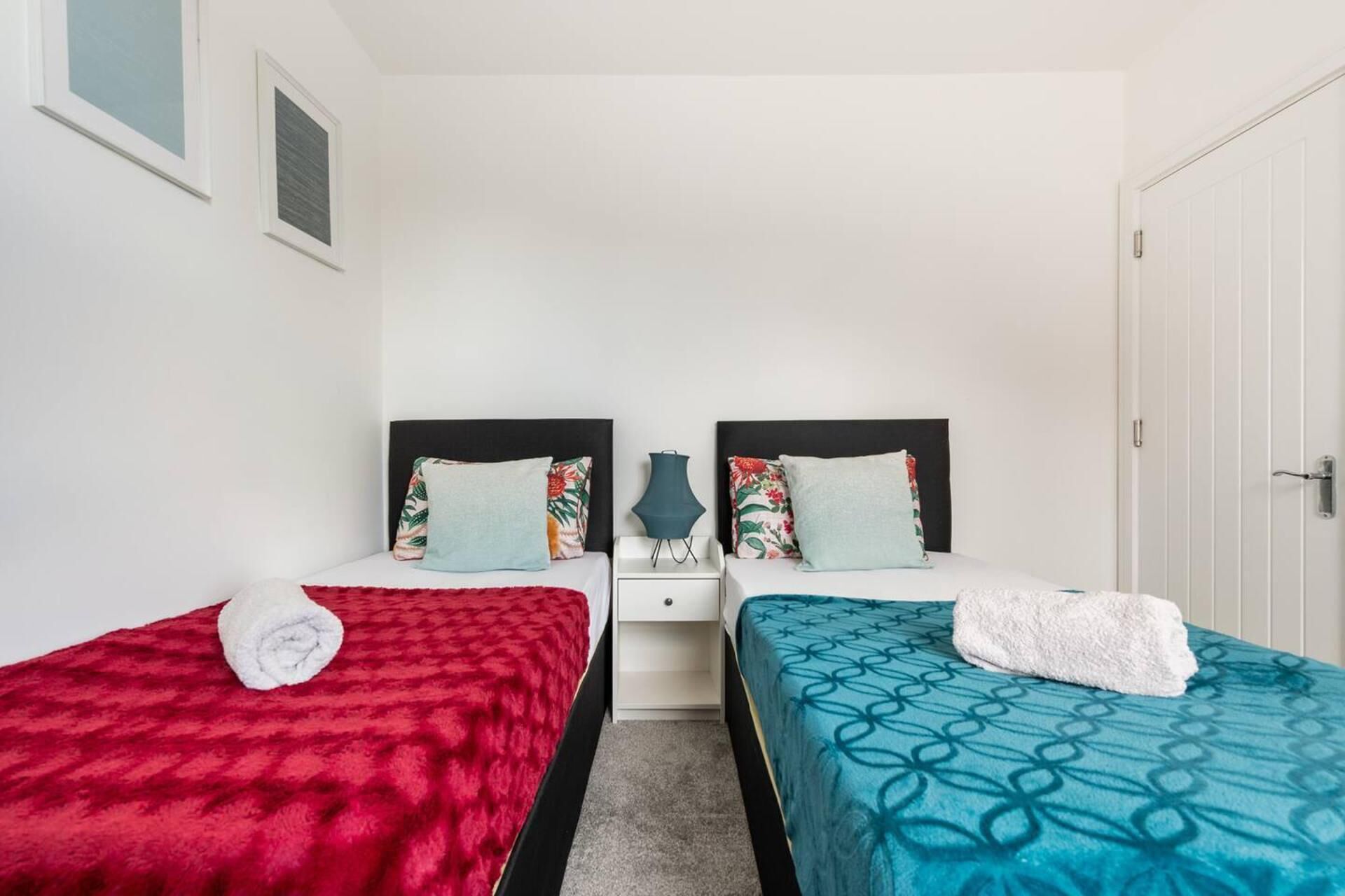 Een tweepersoonskamer met twee bedden, elk met een uniek beddegoed, een nachtkastje en een kleine tafel met een vaas.