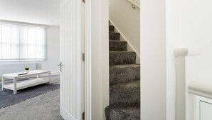 Habitación moderna con una puerta blanca, una escalera con peldaños alfombrados, un radiador blanco y una pequeña mesa blanca con una planta.