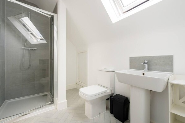 A modern bathroom with a glass-enclosed shower, a white toilet, and a sink with a grey backsplash. - Modern Apartment, Castle View Rochester, England (Rochester)