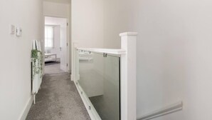 Un pasillo estrecho con cabina de ducha de vidrio, un radiador blanco y una puerta que da a otra habitación.