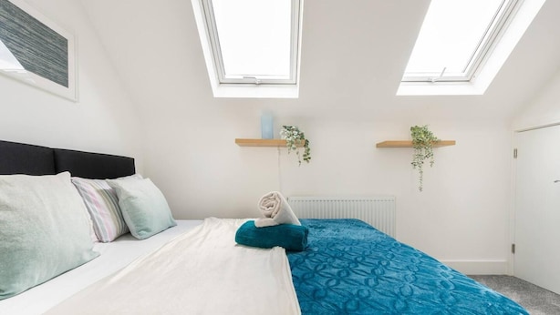Un dormitorio con una cama, un radiador, dos ventanas y dos estantes en la pared con plantas.