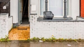 A two-story residential building with a white facade, a bay window on the upper floor, and a small front porch with a bench. - Immaculate 4-bed House Near Anfield and Goodison (Bootle)