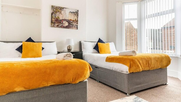 A hotel room with two beds, a painting on the wall, and a window with a view of buildings. - Immaculate 4-bed House Near Anfield and Goodison (Bootle)