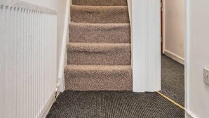 A carpeted staircase in a hallway with white walls and a radiator on the left. - Immaculate 4-bed House Near Anfield and Goodison (Bootle)