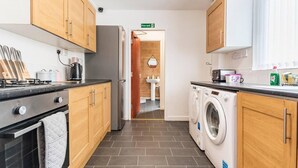 A compact kitchen with wooden cabinets, a stove, a washing machine, and a sink. - Immaculate 4-bed House Near Anfield and Goodison (Bootle)