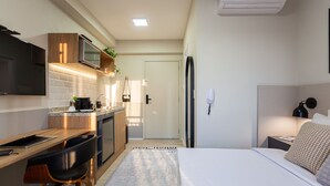 A compact hotel room with a kitchenette, a bed, a desk, and a chair.