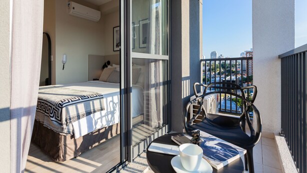 A balcony with a bed, a table with a cup and saucer, and a view of the city.