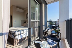Un balcón con una cama, una mesa con una taza y un plato, y vistas de la ciudad.