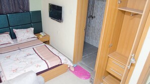 A bedroom with a bed, bedside table, TV, and a wooden wardrobe. - Coolio Hotel & Suites (Lagos)
