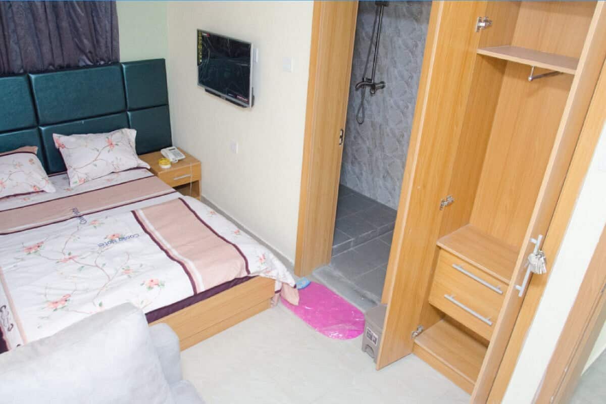 A bedroom with a bed, bedside table, TV, and a wooden wardrobe.