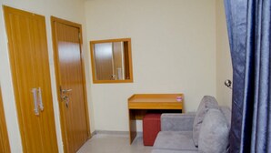 A room with a grey sofa, a wooden desk, and two wooden doors. - Coolio Hotel & Suites (Lagos)