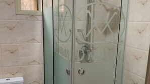 A bathroom with a glass shower enclosure, a toilet, and tiled walls. - Coolio Hotel & Suites (Lagos)