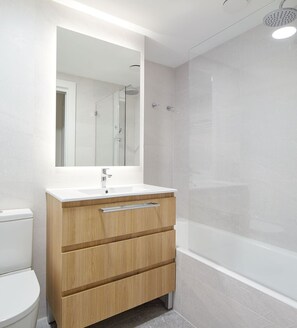 A modern bathroom with a white sink, wooden vanity, and a glass shower enclosure. - Olabar I | The Rentals Collection (San Sebastián)