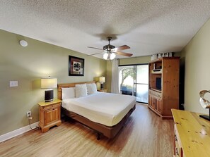 A bedroom with a bed, ceiling fan, wooden nightstands, a wooden wardrobe, and a sliding glass door to the outside.