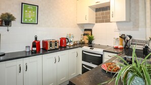A modern kitchen with white cabinets, a black countertop, and stainless steel appliances. There is a framed menu on the wall and a potted plant on the counter. - 5 Thomas Street (Caernarfon)