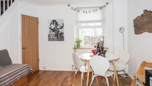 A cozy room with a wooden staircase, a dining area with white chairs, a table with a bottle and glasses, and a framed picture on the wall. - 5 Thomas Street (Caernarfon)