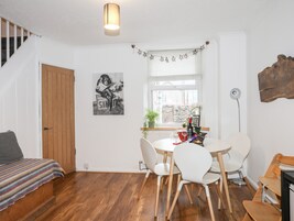 A cozy room with a wooden staircase, a dining area with white chairs, a table with a bottle and glasses, and a framed picture on the wall.