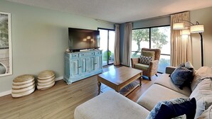 Un salon avec un téléviseur posé sur un meuble, un canapé, une table basse et un fauteuil.