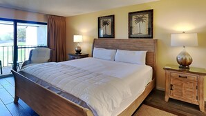 A hotel room with a large bed, two bedside lamps, a wooden nightstand, a chair, and a balcony with a view.