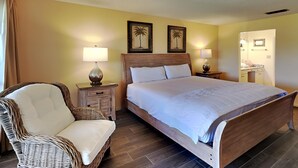 A bedroom with a wooden bed, two bedside lamps, a wicker chair, and two framed pictures on the wall.